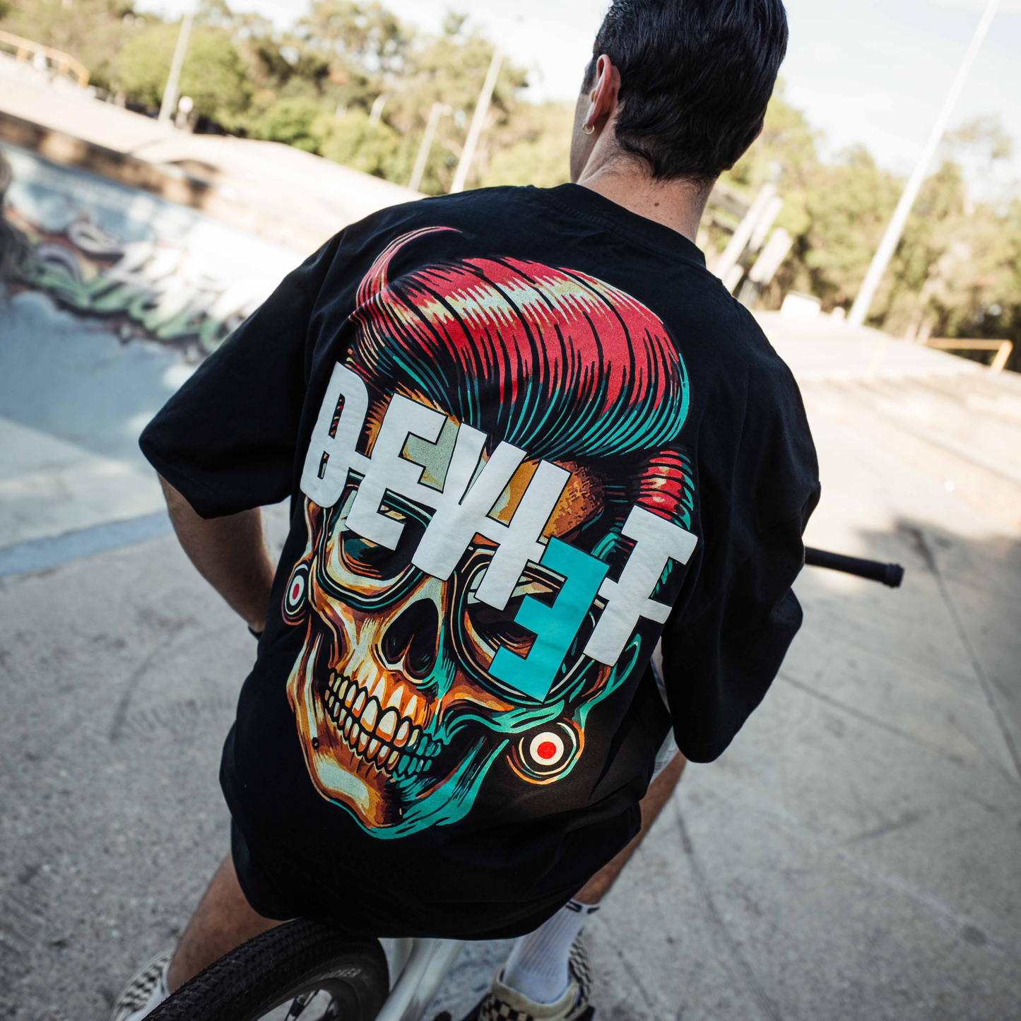 Person on a bike wearing a black t-shirt with a colorful graphic design at a skate park.