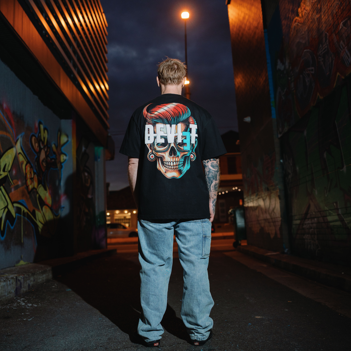 Person wearing a black t-shirt with a colorful skull design in an urban setting at night.
