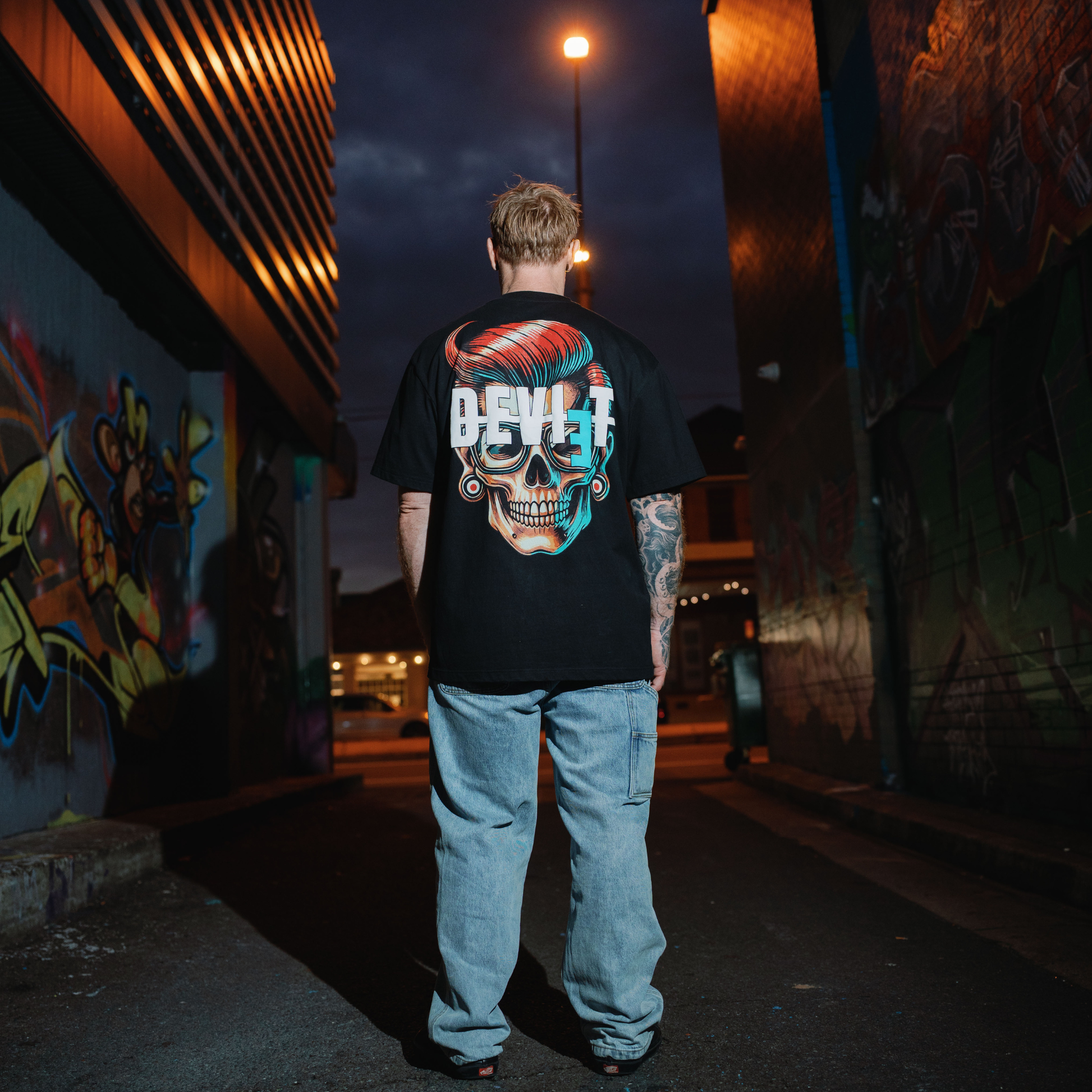 Person wearing a black t-shirt with a colorful skull design in an urban setting at night.