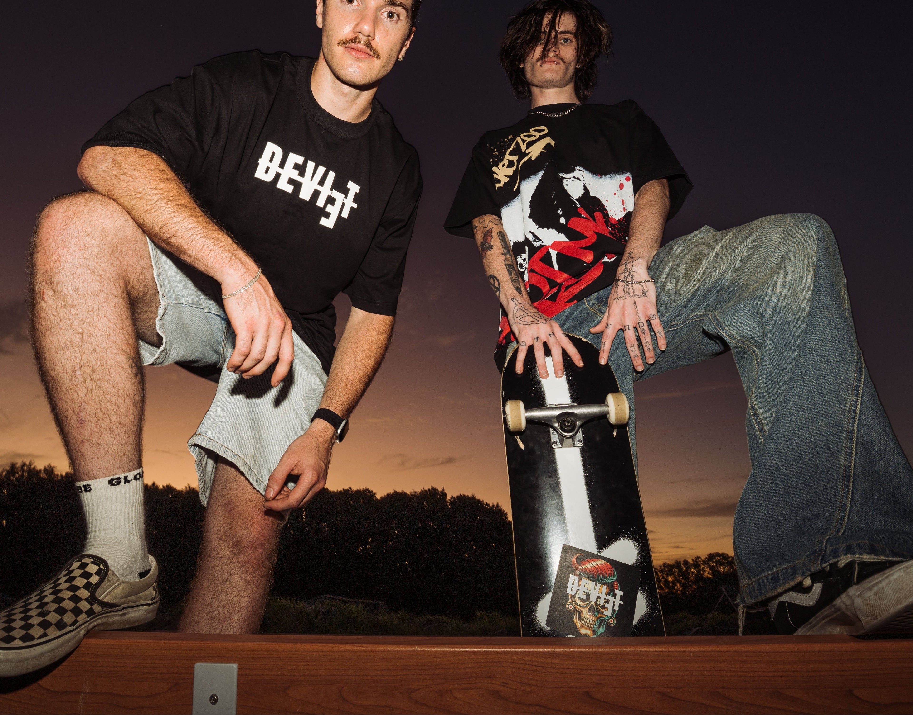 Two individuals with skateboards against a sunset sky